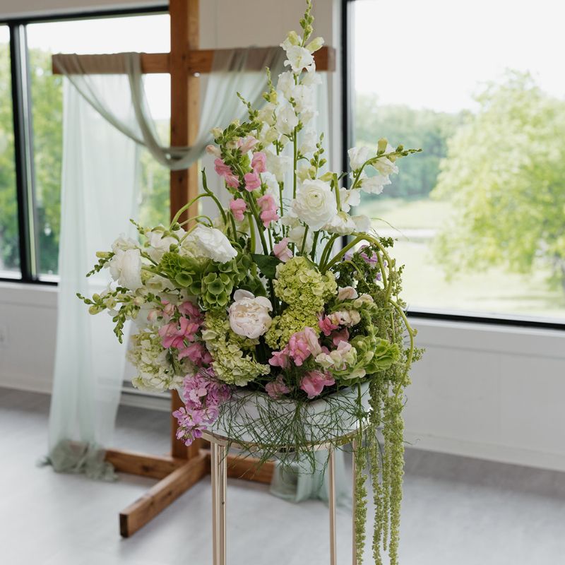 Large pink and green floral altar arrangement in front of a fabric-draped cross
